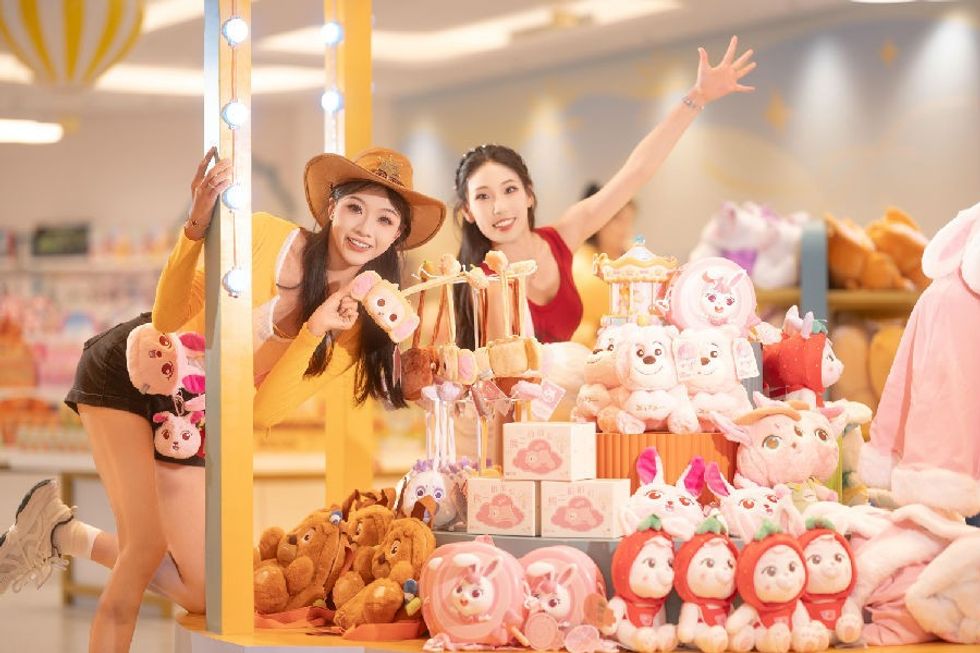 Two women smiling by a display of colorful plush toys in Fantawild store