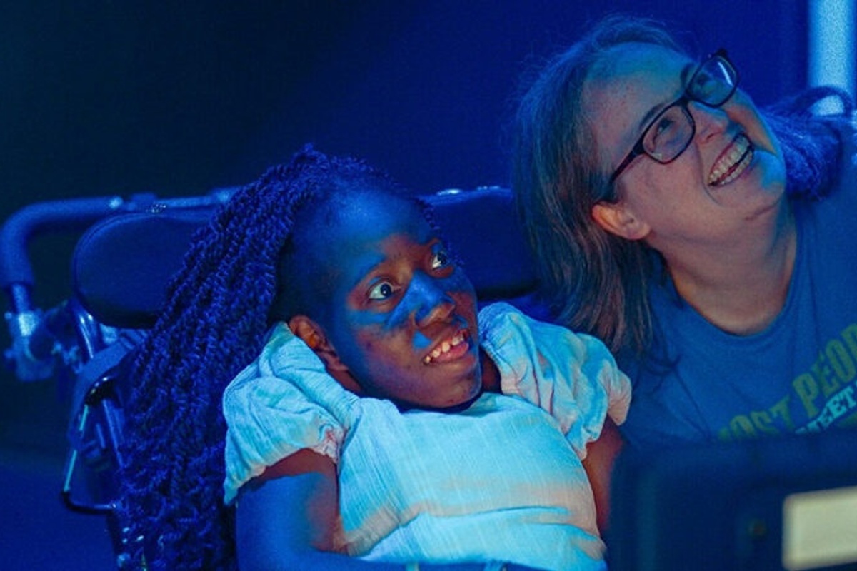 Two women smiling under blue lighting, one in a wheelchair.