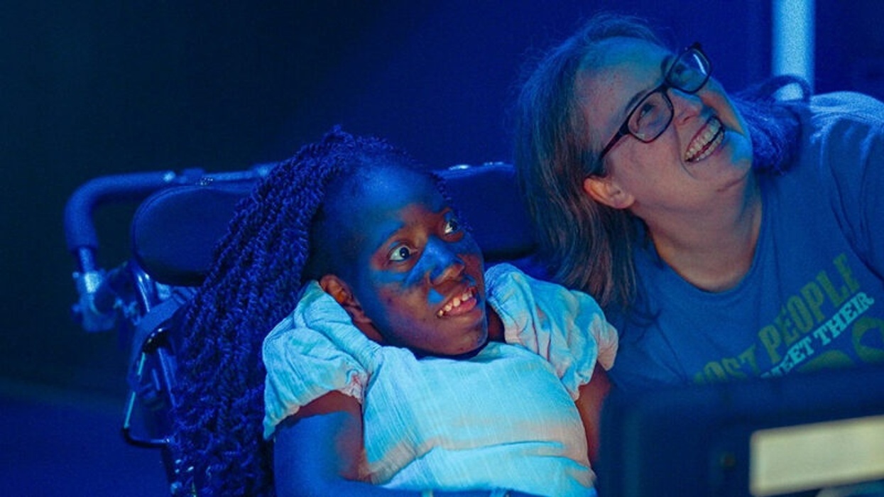 Two women smiling under blue lighting, one in a wheelchair.