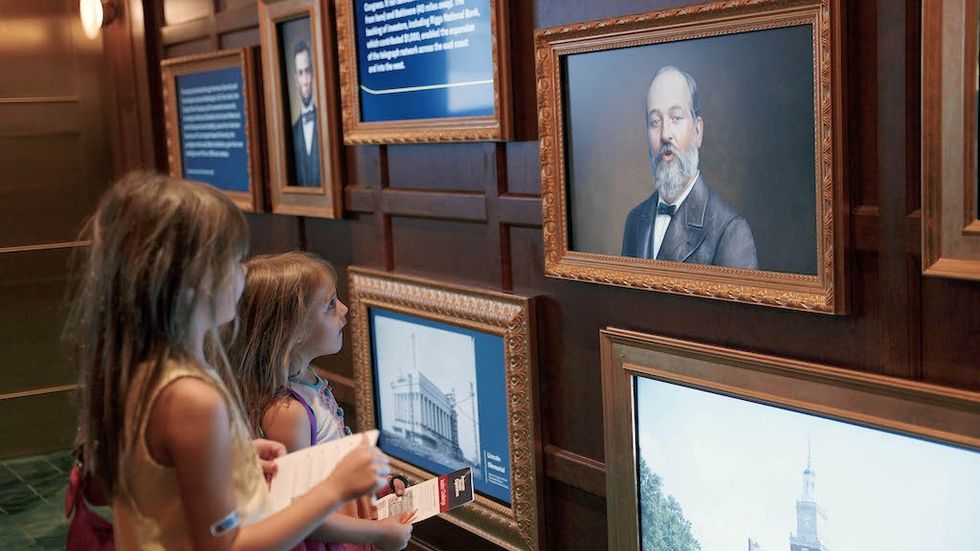 Two young girls viewing historical portraits and texts on a museum wall.