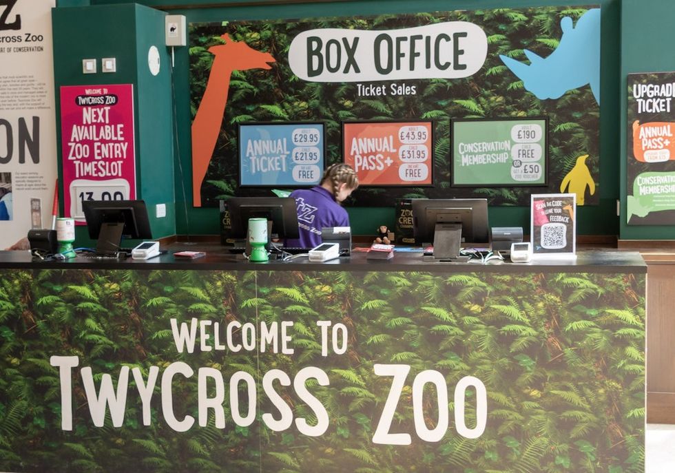 Twycross Zoo box office with ticket prices and a staff member at the counter.