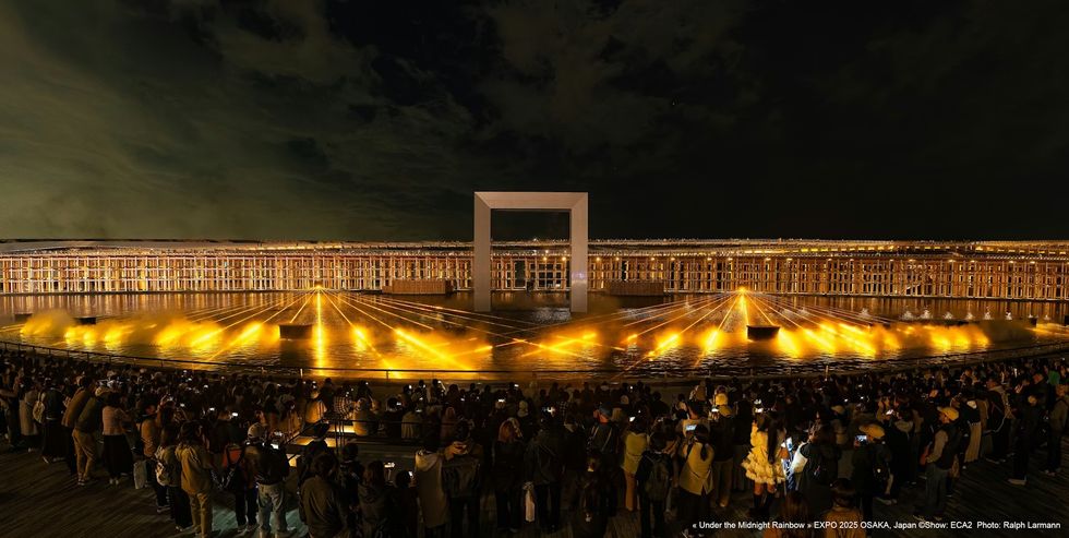 Under The Midnight Rainbow ECA2 Crowd watches a vibrant nighttime water and light show with a large frame structure.