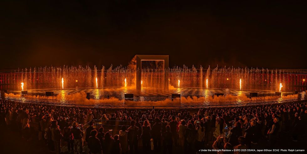 Under The Midnight Rainbow ECA2 Crowd watching a night water and fire show with flaming fountains and a large illuminated frame.