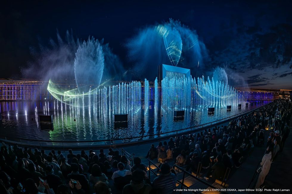 Under The Midnight Rainbow ECA2 Spectacular water and light show at night over a crowded outdoor venue.