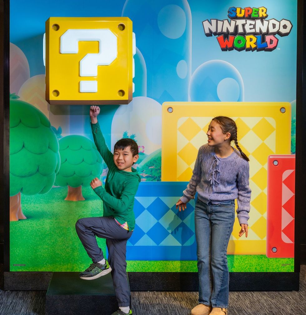Universal Theme Parks: The Exhibition - two kids pose joyfully by a Super Nintendo World backdrop with question block.