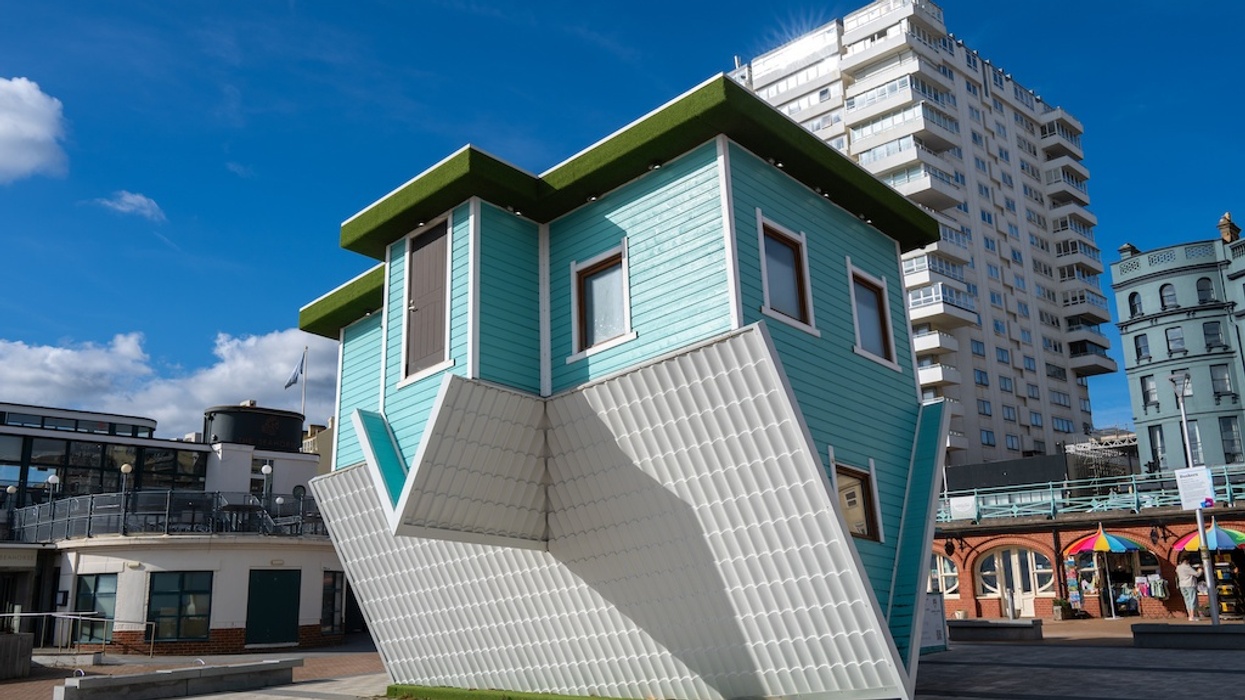 Upside-down turquoise house on a plaza with a clear blue sky background.