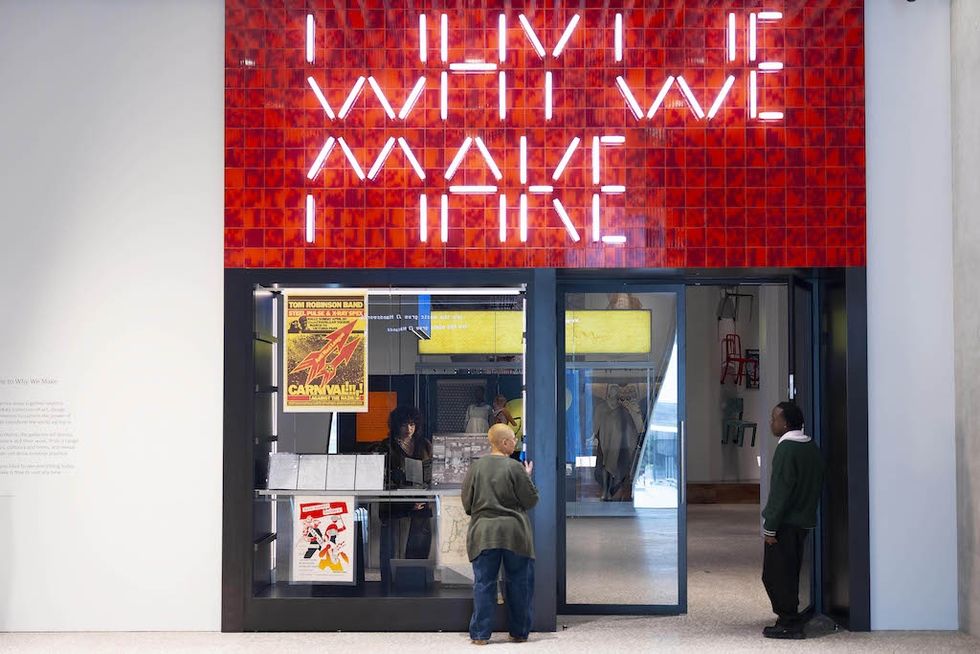 V&A East gallery entrance with neon sign "WHY WE MAKE," two people, posters, and interior decor visible.