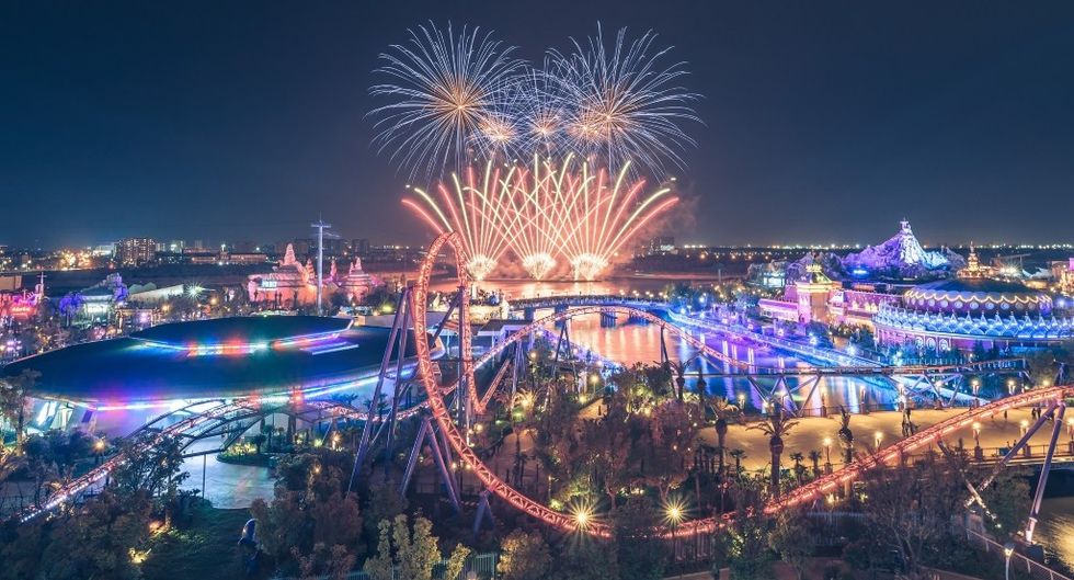 Vibrant amusement park at night with fireworks lighting up the sky.
