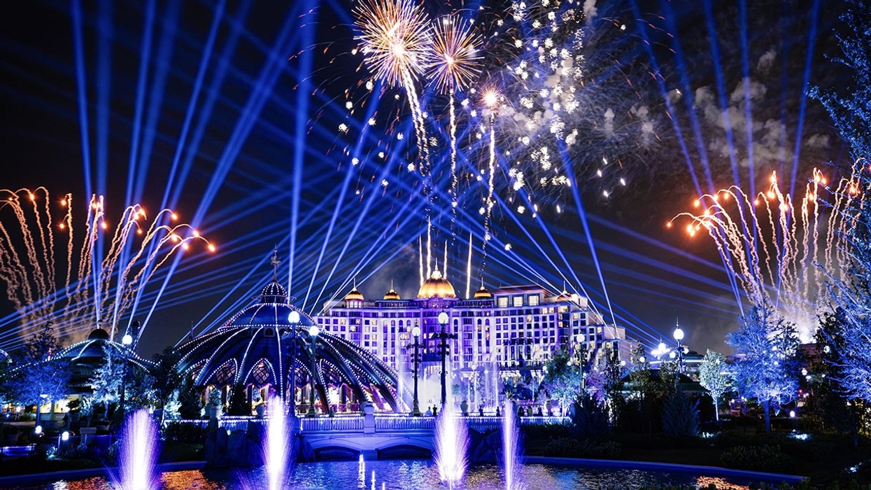 Vibrant fireworks and laser show above a lit building and fountains at night.