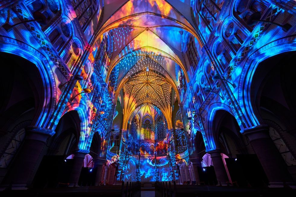 Vibrant light projections illuminate intricate cathedral arches in vivid blues and golds.