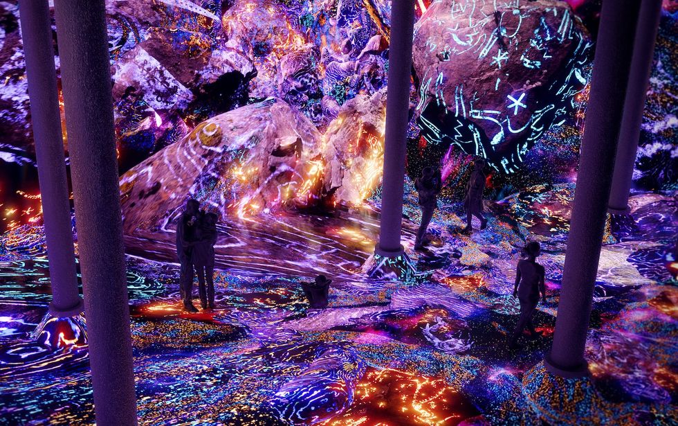 Vibrant, neon-lit cave with people walking among glowing, intricately patterned rocks at Artechouse