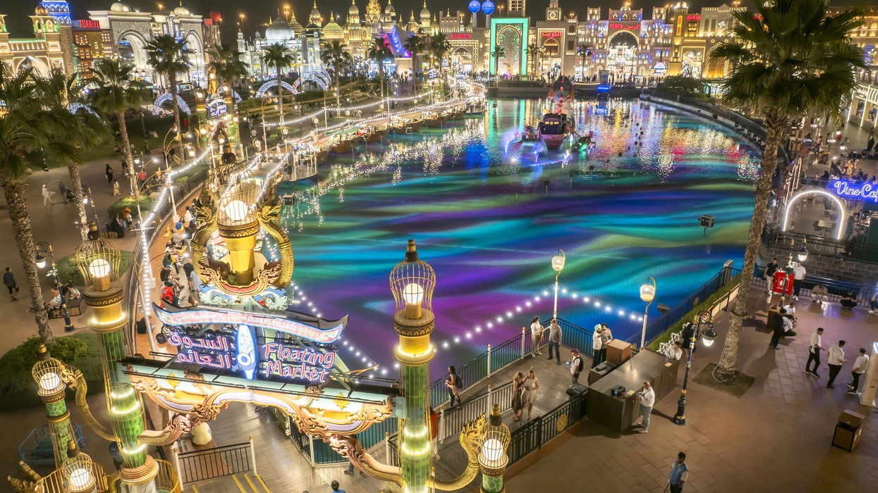 Vibrant night scene of a lit-up floating market called Global Village with colorful water reflections.