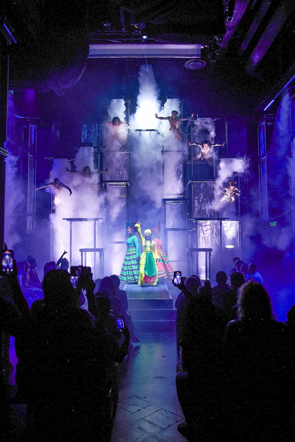 Vibrant stage performance with colorful costumes and dramatic smoke effects.