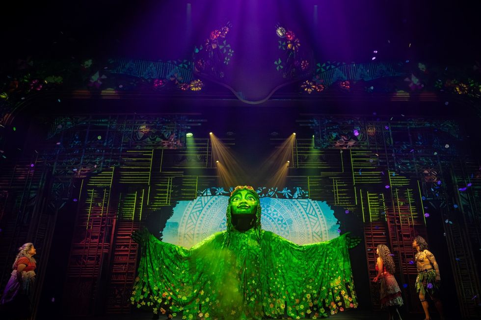 Vibrant stage scene with a giant green figure and performers in colorful costumes.