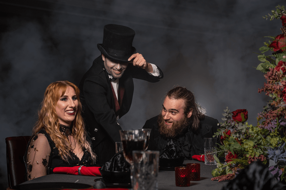Victorian-themed dinner party at Alton Towers with three people laughing, surrounded by flowers and candles.