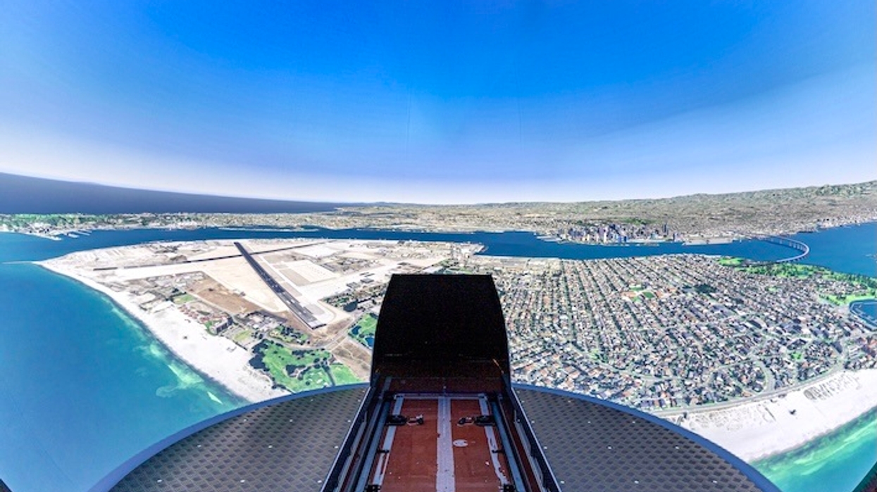 View of coastline and city from a flight simulator cockpit with clear blue sky.