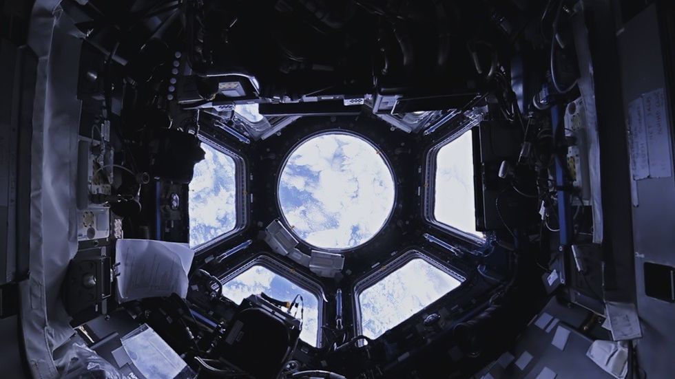View of Earth from space through a circular window inside a spacecraft.