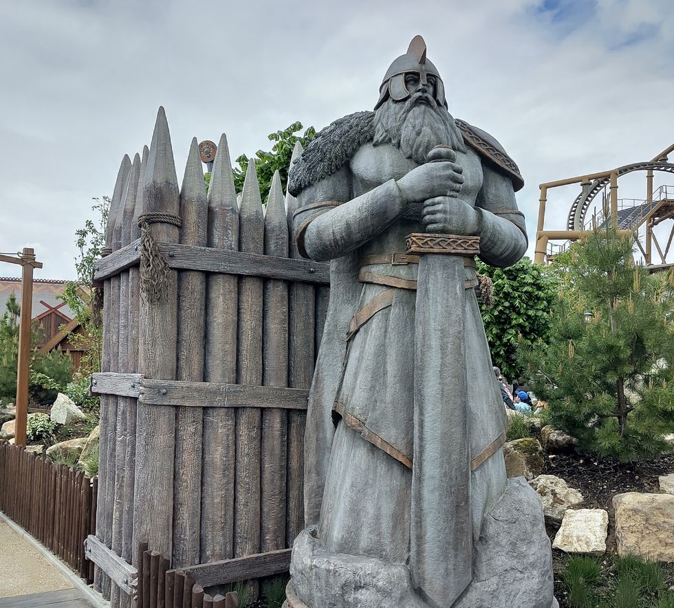 Viking statue with a sword by a wooden fence, under a cloudy sky.
