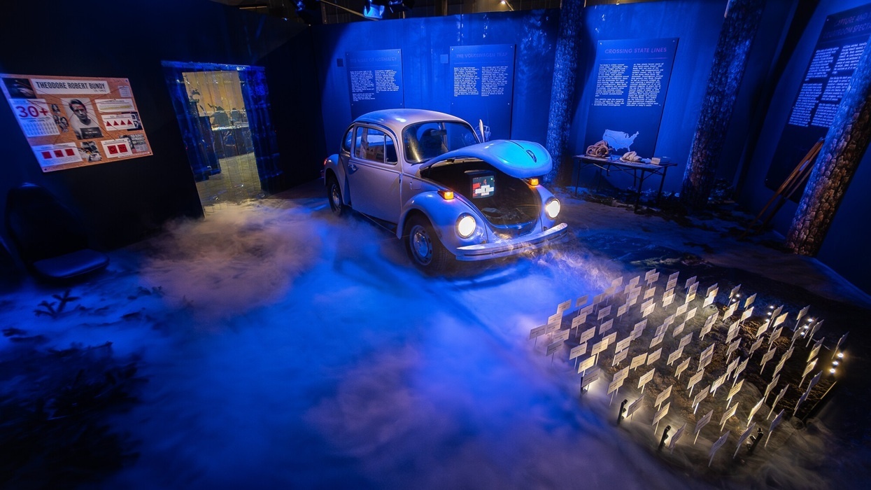 Vintage car exhibit in moody blue lighting with smoke and informational panels, in The Mind of a Serial Killer: The Experience.