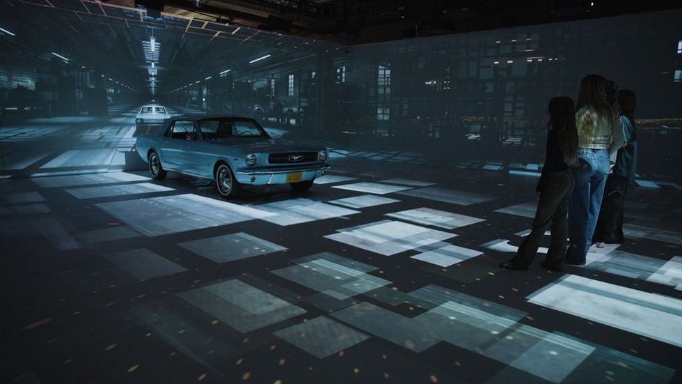 Vintage car in a digital art space, with projections and people observing.