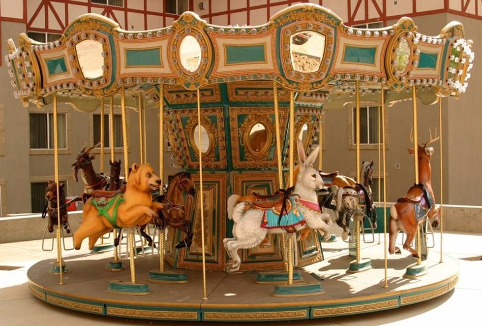 Vintage carousel with animal figures in a sunlit courtyard.