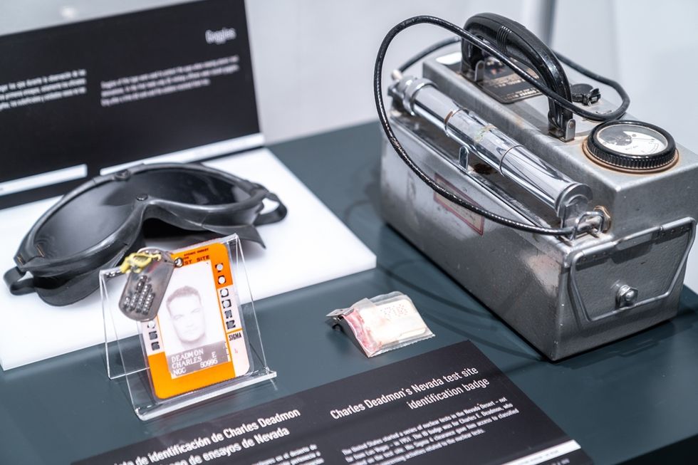 Vintage goggles, ID badge, and a geiger counter displayed on a table with descriptive labels.