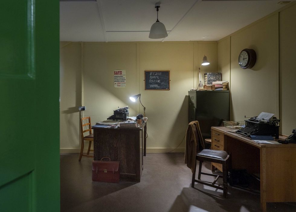 Vintage office with typewriters, desk lamps, and a clock on a beige wall at Bletchley Park