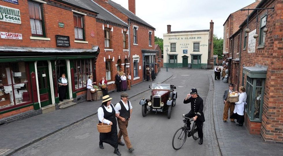 Vintage street scene with people, an old car, and a policeman on a bicycle at Black Country Living Museum