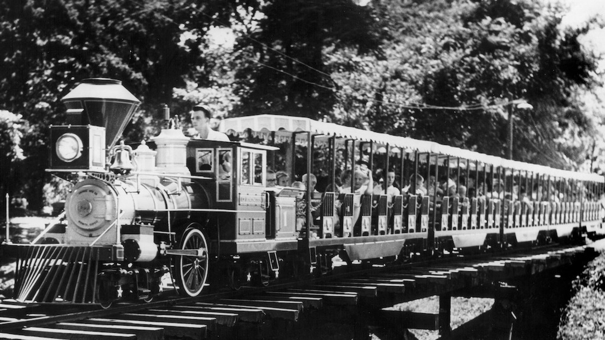 Vintage train with passengers crossing a wooden bridge, surrounded by trees.