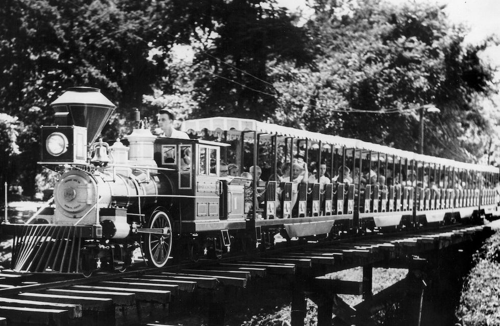 Vintage train with passengers crossing a wooden bridge, surrounded by trees.