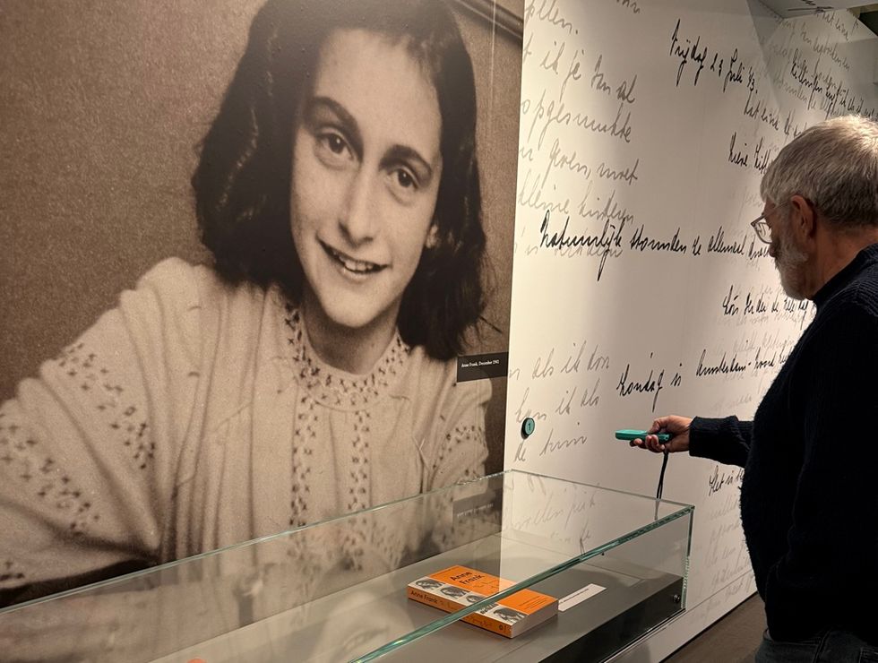 Visitor examines a display in front of a large photo of Anne Frank at a museum, using Podcatcher Pro audio guide frm Guide-ID