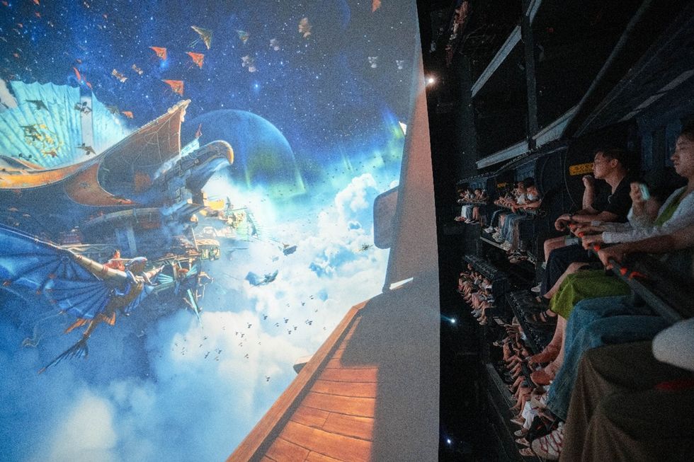 Visitors sit in rows watching a large immersive screen depicting a ship floating among clouds and planets, in Mountains and Seas