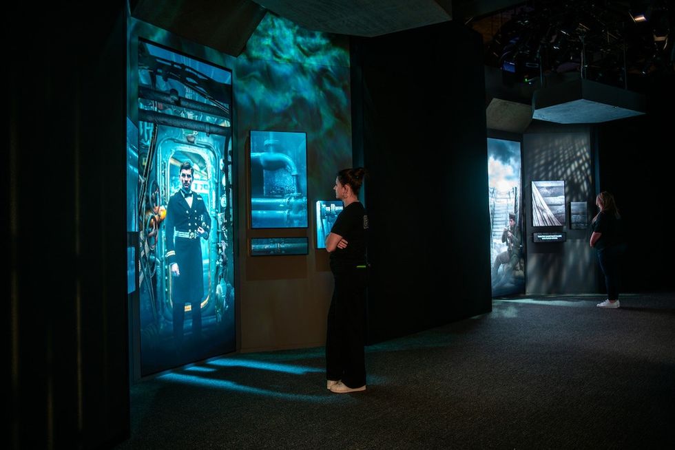 Visitors view immersive digital displays at a dark, modern exhibition.