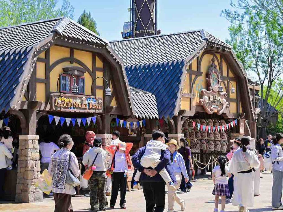 Visitors walk past wooden shops with steep tiled roofs at POP LAND