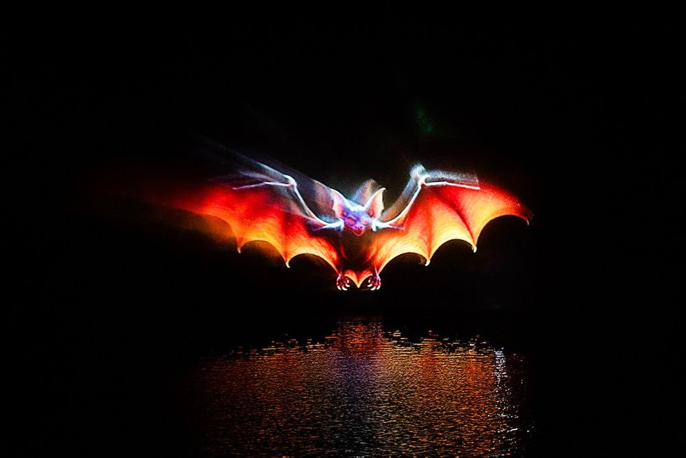 Vivid holographic bat with glowing wings above reflective water in darkness.