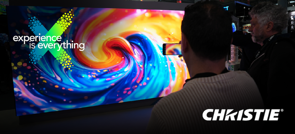 Vivid swirl display with "Experience is Everything" text and Christie logo, seen by two people at a showcase.