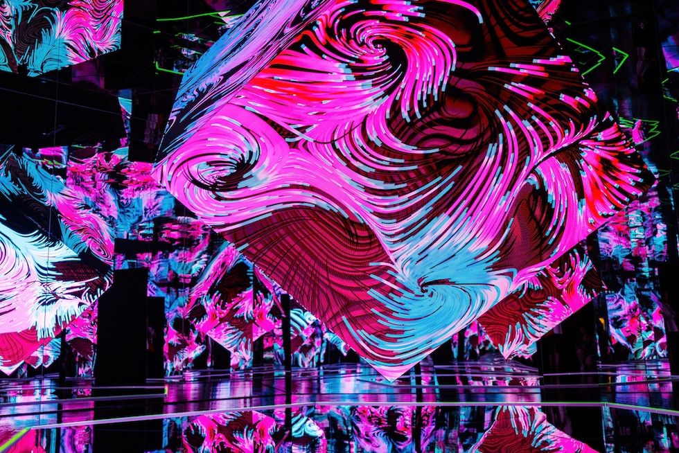Vivid swirling light patterns on large cubes, creating an immersive digital art display.