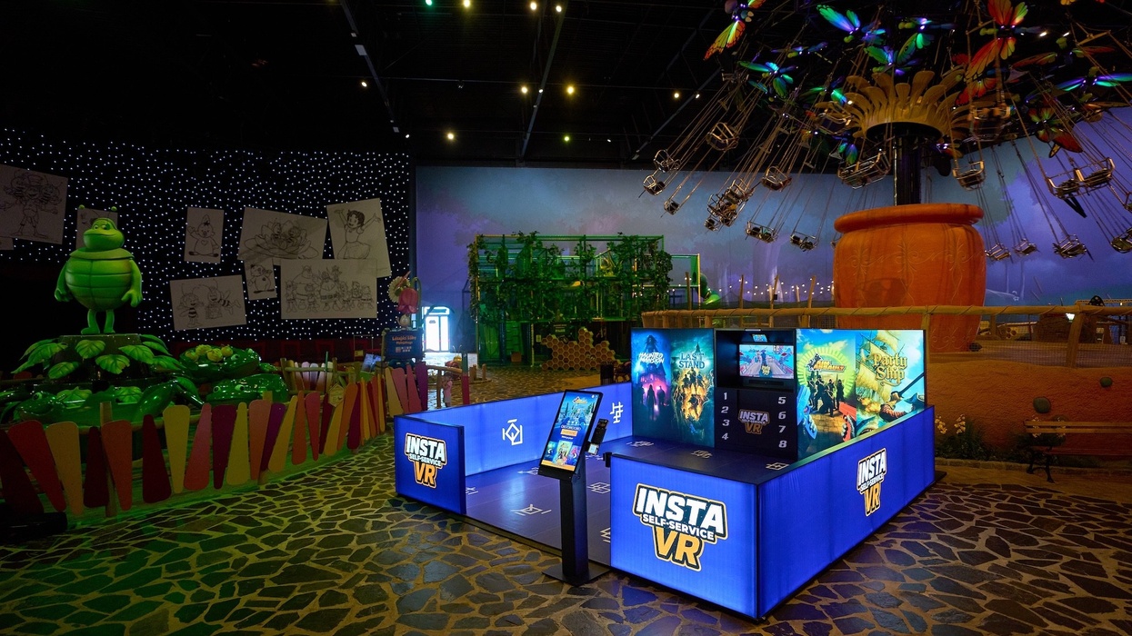 VR gaming booth in a colorful amusement park with a swing ride and green character nearby.