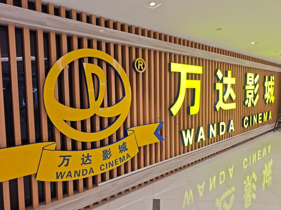 Wanda Cinema bright yellow signage on a wooden slat wall indoors.
