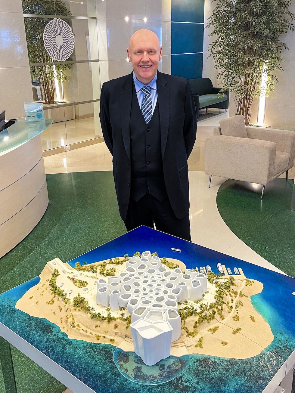 Warren Baverstock in suit standing by architectural island model for Corallium, in modern office.