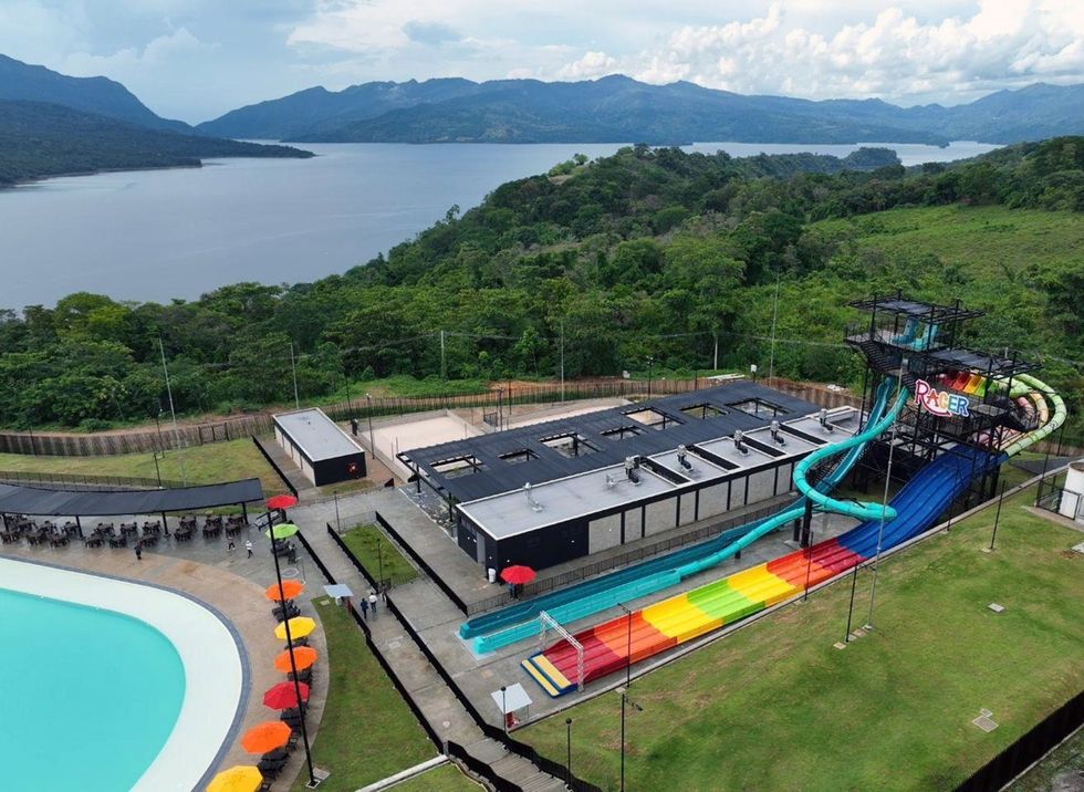 Water park with colorful slides and pool, surrounded by greenery with a lake and mountains beyond.