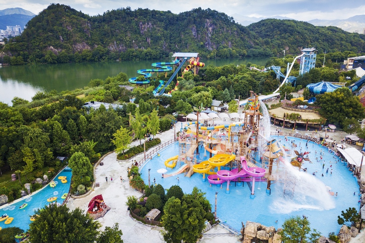 Water park with colorful slides surrounded by lush greenery near a scenic lake.
