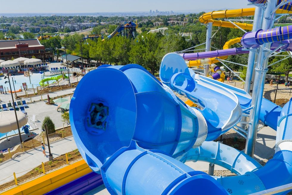 Water park with winding blue and yellow slides, overlooking a pool area and trees.