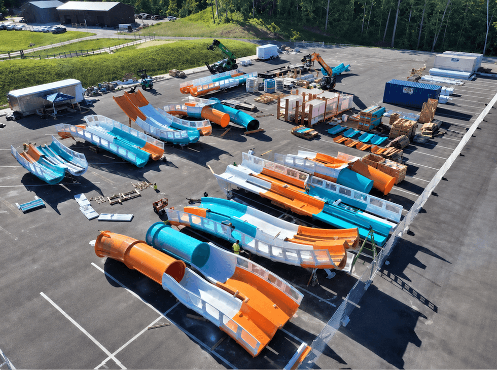 Water slide sections in various colors assembled in a parking lot, with construction equipment.
