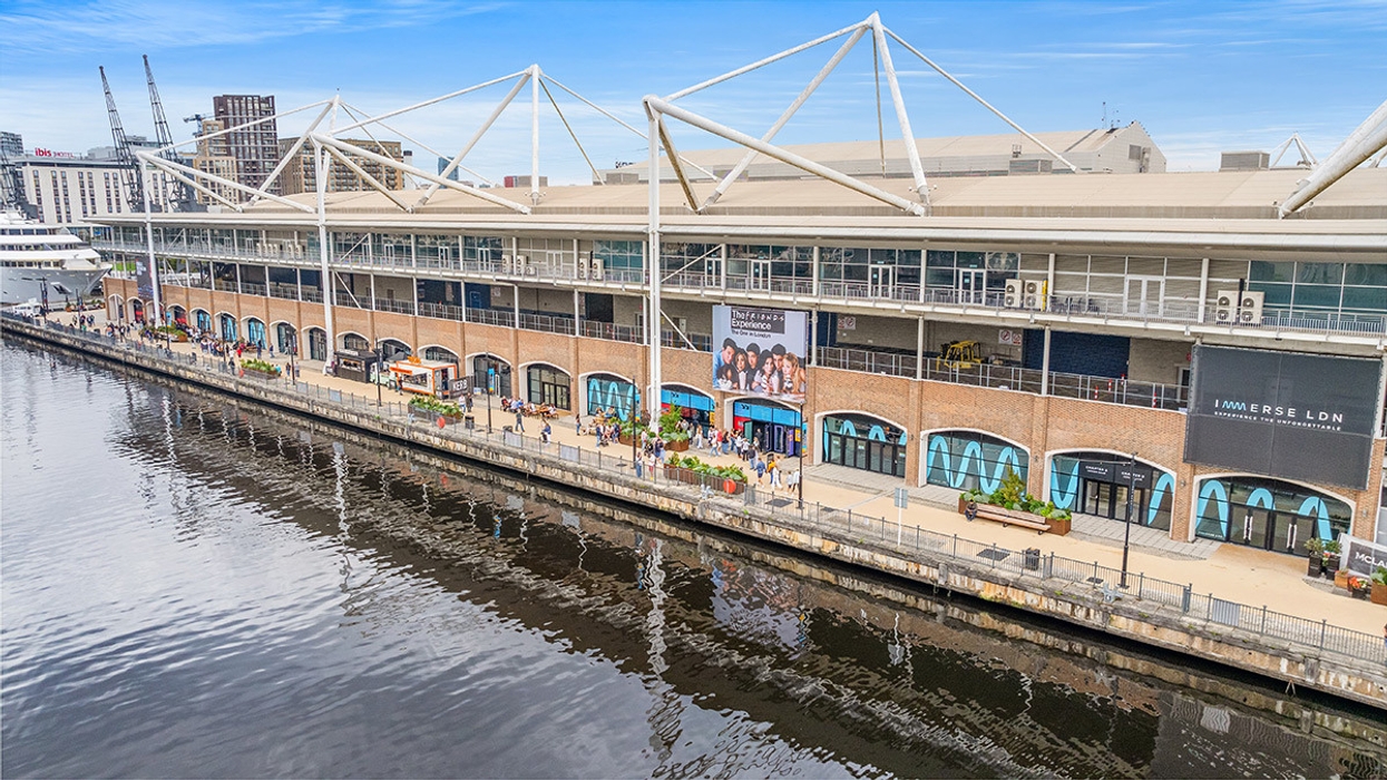 Waterfront building with large windows and people walking along a promenade under a clear sky.
