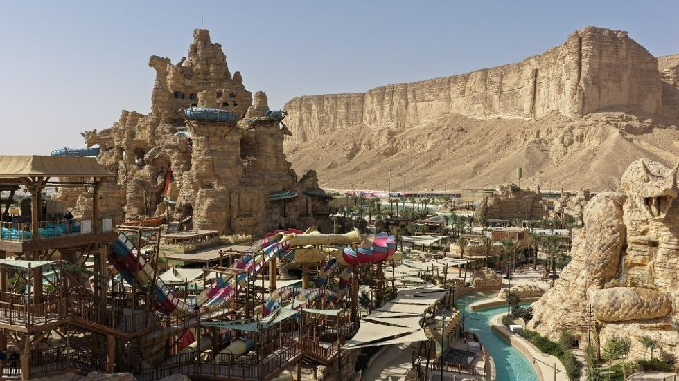 Watery amusement park with colorful slides, surrounded by desert cliffs under a clear sky.