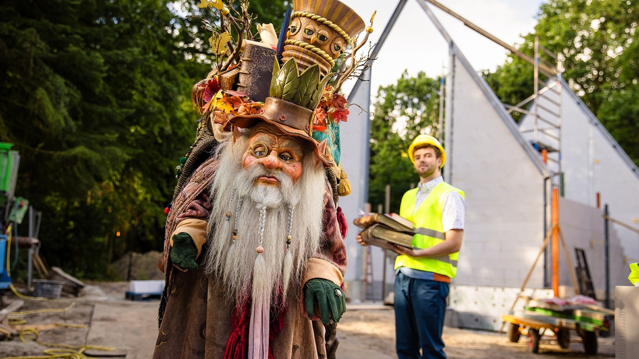 Whimsical character in costume near a construction site with a worker in the background at Efteling