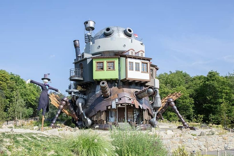 Whimsical walking house with mechanical legs and scarecrow, surrounded by greenery.