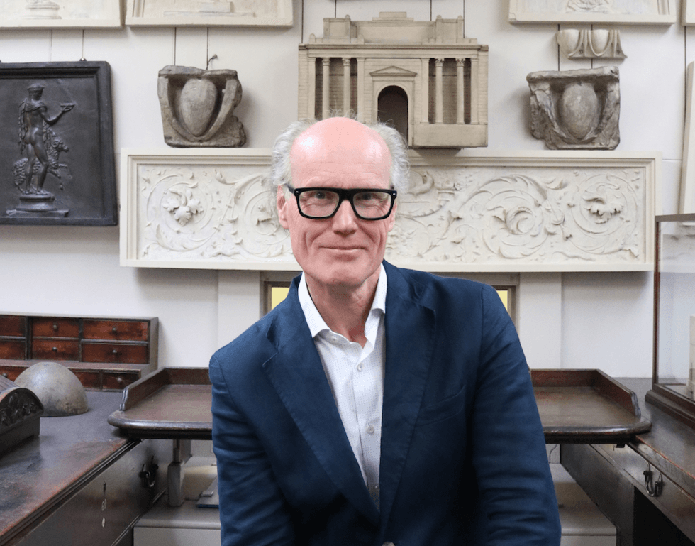 Will Gompertz surrounded by classical architectural artifacts.