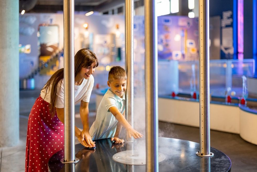 Woman and boy exploring a science exhibit with mist and metal poles.